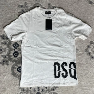 Vit DSQUARED2 t-shirt med tryck - Vit t-shirt från DSQUARED2 i mjuk bomull med svart DSQ-tryck nere vid fållen. Klassisk rund halsringning och korta ärmar. Enkel men ändå riktigt snygg, perfekt för dig som gillar stilrena plagg med en twist.