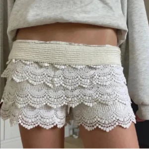 spets shorts - Superfina vita shorts med flera lager volang i spets och broderade detaljer. Bred resår i midjan för skön passform. Perfekta till sommaren när du vill ha något både gulligt och bekvämt.