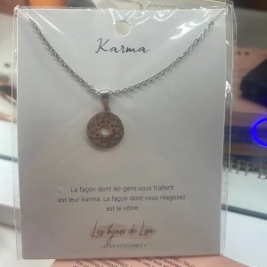 Karma halsband från Les bijoux de Lisa - Helt ny, ifrån nice/ frankrike. Snyggt halsband i silverfärg med en rund, geometriskt mönstrad berlock. Kedjan är tunn och stilren, perfekt för dig som gillar minimalistiska smycken med en spirituell touch. Berlocken har ett öppet cirkelmönster som ger ett modernt och unikt intryck
