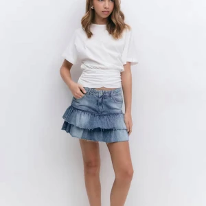  Jeanskjol från Young Gina str 152  - Supersöt kort jeanskjol i blå med två lager volanger och råa kanter. Från Young Gina str 152. Helt slutsåld på hemsidan! Säljer för att den inte används. Avänd 1 gång. Kan sänka priset.