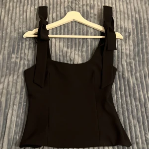 Svart linnetopp med rosetter 🖤 - Supersnygg svart linnetopp från Zara med breda axelband som knyts i rosetter, storlek S. 🎀Helt ny, använt den en gång när jag provade den. Säljer endast för att den var för liten för mig. Hann riva av kappen innan jag provade toppen, så den sitter inte kvar. 🥰