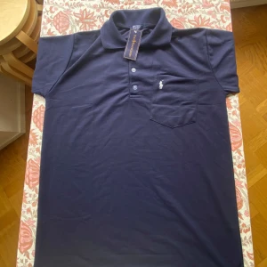 Marinblå pikétröja från Ralph Lauren - Snygg marinblå pikétröja från Ralph Lauren med klassisk krage, knäppning med tre knappar och bröstficka med broderad logga. Tillverkad i mjuk bomull, perfekt för en stilren look.