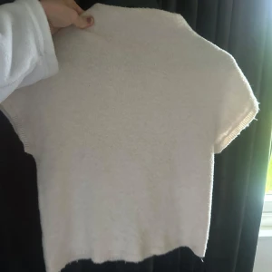 Ljusbeige stickad kortärmad tröja - Enkel och stilren ljusbeige stickad tröja med korta ärmar. Tröjan har en rak passform och ribbade kanter vid ärmslut och nederkant. Perfekt för lager-på-lager eller sommarens svalare dagar.