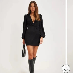 Svart omlottklänning från Nelly - Supersnygg svart kort omlottklänning från Nelly med djup v-ringning och långa puffärmar. Klänningen har en lätt strukturerad yta och markerad midja. Använd ett fåtal gånger. Sälj inte längre på Nelly. Nypris 499kr