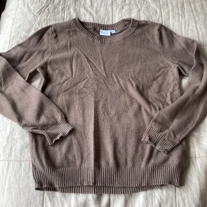 Brun stickad tröja från VILA - Mysig brun stickad tröja från VILA i storlek L. Tröjan har rund halsringning, långa ärmar och breda ribbade muddar vid ärmslut och nederkant. Nopprig. 