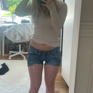 Lågmidjade jeansshorts från Blend - Snygga blå jeansshorts från Blend med super låg midja och råa kanter. Shortsen har slitna detaljer, klassiska fickor fram och bak samt bälteshällor. Perfekta för sommardagar när du vill ha en avslappnad och trendig look. 