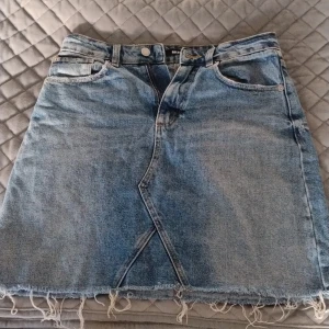 Jeanskjol från Bik Bok med fransig kant - Snygg blå jeanskjol från Bik Bok i klassisk modell med fem fickor, fransig nederkant och cool omlott-detalj framtill. Kjolen har bälteshällor och slitna detaljer baktill för en avslappnad vibe. OBS! Det är riktiga fickor!