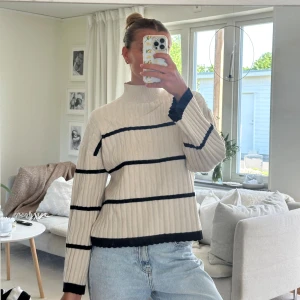 Beige randig stickad tröja från Pieces - Säljer en beige stickad tröja från Pieces med svarta horisontella ränder. Tröjan har hög hals, långa ärmar och ribbad struktur. 