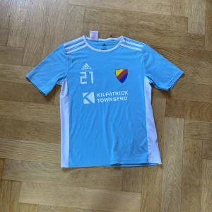 Ljusblå Djurgården fotbollströja Adidas - Snygg ljusblå fotbollströja från Adidas med Djurgårdens IF klubbmärke och nummer 21 på bröstet. Tröjan har vita detaljer på axlar och sidor, samt flera sponsorer tryckta fram och bak. Tillverkad i lätt och ventilerande Climalite-material.