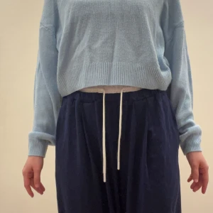 Ljusblå stickad croppad tröja - Supermjuk ljusblå stickad tröja med croppad passform och bred ribbad kant nertill. Tröjan har långa ärmar och en avslappnad, loose siluett som ger en chill vibe. Perfekt att styla med höga byxor eller kjol för en trendig look. 