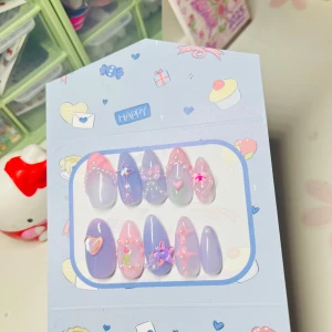 Lila och rosa press-on naglar med 3D-dekorationer - Säljer ett set med långa, mandelformade press-on naglar i lila och rosa nyanser. Naglarna har 3D-dekorationer som pärlor, stjärnor, hjärtan och fjärilar samt handmålade detaljer. Perfekt för dig som vill ha en söt och unik look med extra bling.