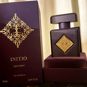 Initio Side Effect Eau de Parfum - Lyxig parfymflaska från Initio, Side Effect, 90 ml. Flaskan är mörklila med en fyrkantig form och har en elegant guldfärgad dekor på framsidan. Kommer i exklusiv ask med matchande guldmönster. Perfekt för dig som gillar unika och sofistikerade dofter.