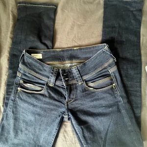 Mörkblå straight jeans från Pepe Jeans - Snygga mörkblå jeans från Pepe Jeans i modellen Venus med raka ben och låg midja. Klassisk femficksdesign, kontrastsömmar och detaljerade bakfickor. Jeansen är gjorda i mjukt denimtyg och har en stilren look som passar till allt.