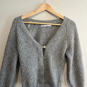 Grå stickad kofta från Only - Säljer en mysig grå stickad kofta från Only med v-ringning och knappar framtill. Perfekt för kyliga dagar med sin ribbade design och långa ärmar. En stilren och bekväm tröja för alla tillfällen. Storleken är lik XS förutom lite kortare ärmar.