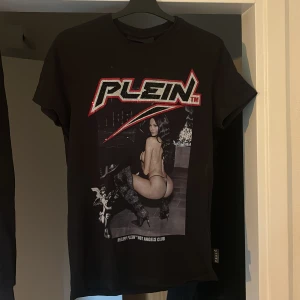 Svart Philipp Plein t-shirt med tryck - Cool svart t-shirt från Philipp Plein med stort grafiskt tryck framtill och text på ryggen. T-shirten har korta ärmar och klassisk passform. Materialet är mjuk bomull och trycket har detaljer i rött och vitt. Perfekt för dig som vill sticka ut med edgy streetstyle.