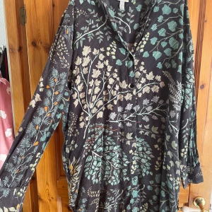 Blommig skjorta från Dedicated - Snygg skjorta från Dedicated med svart botten och blommigt mönster i grönt, beige och lite orange. Skjortan har lång ärm, knappar framtill och avslappnad passform. Tillverkad i mjukt material som känns skönt mot huden.