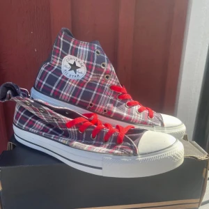 Rutig Converse All Star med röda snören - Oanvända snygga Converse All Star high-tops i röd, vit och mörkblå rutig bomull. Skorna har klassisk vit gummisula, rund tå och coola röda snören som sticker ut. Perfekta för dig som vill ha en unik twist på dina sneakers.