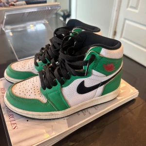 Nike Air Jordan 1 Retro lucky green - Säljer ett par Nike Air Jordan 1 Retro med grön, vit och svart färg. Skorna har svart snörning, klassisk svart swoosh och röd Air Jordan-logga på sidan. Ovandelen är i skinn med perforerad tåbox och högt skaft. Perfekta för dig som vill sticka ut med din sneakerstil.