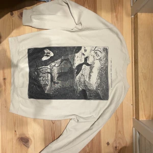 Beige sweatshirt Les Voyages Extraordinaires - Snygg beige sweatshirt från Vintage Supply med tryck fram och bak. Framsidan har texten 'Les Voyages Extraordinaires' och baksidan har en stor svartvit grafisk print med havsmotiv. Mjuk bomullskänsla och avslappnad passform med långa ärmar. Perfekt för en sen sommarkväll 