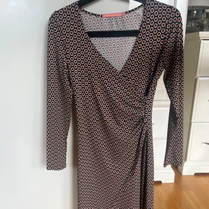Mönstrad omlottklänning Pernilla Wahlgren - Säljer en snygg omlottklänning från Pernilla Wahlgren med svart botten och cirkelmönster.  Klänningen har v-ringning, långa ärmar och knyt/rynk i midjan.