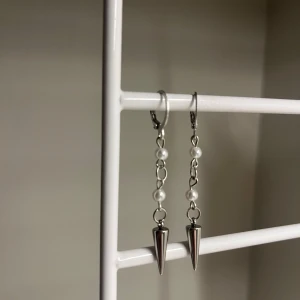 Silvriga örhängen med pärlor och spikes - Rostfritt stål. Snygga hängande örhängen i silverfärg med kedja, små vita pärlor och coola konformade spikes längst ner. Perfekt accessoar för att ge din look en edgy touch. Passar dig som gillar att sticka ut med detaljer. Handgjort 