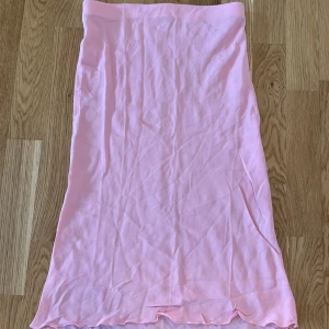 Ljusrosa långkjol i bomull - Söt ljusrosa långkjol i mjukt bomullstyg. Kjolen har en enkel och rak modell med lätt vågig nederkant. Perfekt för dig som gillar en clean och feminin stil.