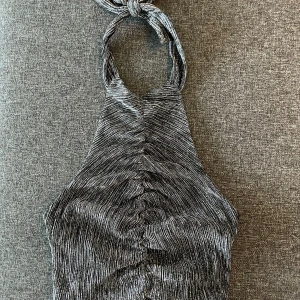Glittrig halterneck topp med knyt - Snygg glittrig halterneck topp i svart och silver med smala ränder och knyt i nacken. Endast använd en gång. Perfekt till fest!🙌