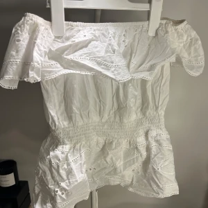 Vit offshoulder blus från Primark - Supersöt vit offshoulder blus från Primark med broderade detaljer och volangkant. Blusen har smock i midjan för en snygg passform och är tillverkad i lätt bomull. Perfekt för varma dagar när du vill ha en romantisk och luftig look.
