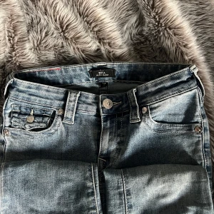 True Religion Jeans - Säljer ett par snygga ljusblå jeans från True Religion, modell Becca Mid Rise Bootcut. Klassisk femficksdesign med ikoniska bakfickor och silverfärgade knappar. Jeansen har en bootcut-passform och coola kontrastsömmar. Skulle även kunna vara öppen till att byta till ett par w24 ❣️sparsamt använda och har inga slitningar eller liknande. Kommer från ett rökfritt hem men har pälsdjur!❣️