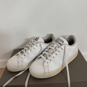 Vita Adidas Stan Smith sneakers - Klassiska vita Adidas Stan Smith sneakers i skinn med perforerade detaljer på sidorna och vit sula. Skorna har rund tå, snörning och diskret Adidas-logga på plösen. Perfekt för en clean och tidlös stil.