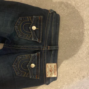 True Religion bootcut jeans mörkblå - Mörkblå bootcut jeans från True Religion med ikoniska bakfickor och kontrastsömmar. Klassisk femficksmodell med låg midja och snygga detaljer, dem har färg fläckar längst ner på benen okej en tråd lös därför 660 köpt för 1499 den är uppsydd så att den passar någon för 165 men jag kan ta bort den så att den är den vanliga längden 