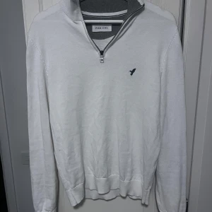 Vit half zip tröja från Pier One - Vit långärmad tröja från Pier One med half zip och liten broderad fågel på bröstet. Tröjan har ribbade muddar och krage i grått, vilket ger en clean och stilren look. Perfekt för lager-på-lager och chill vardagsstil.