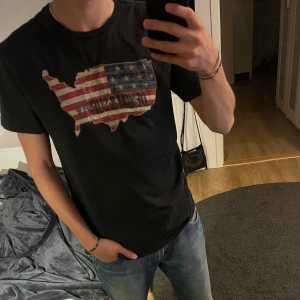 Mörkgrön t-shirt Denim & Supply Ralph Lauren - Mörkgrön t-shirt från Denim & Supply Ralph Lauren med tryck av USA-karta i amerikanska flaggans färger och texten 'DENIM & SUPPLY' på bröstet. Klassisk passform och rund hals. Tillverkad i 100% bomull, perfekt till jeans.