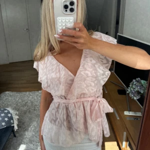 Ljusrosa blus med knytning - Söt ljusrosa mönstrad blus med knytning och volanger. Saknar lapp men gissar på storlek S, jag är 170 cm lång och bär oftast XS och S