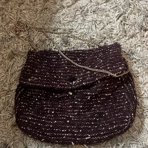 Mörklila axelväska från Beck Söndergaard - Snygg axelväska i mörklila från Beck Söndergaard med guldigt kedjeband. Väskan är stickad med vita prickar och har ett blått innerfoder. Perfekt för dig som vill ha en unik och trendig accessoar med cool textur och detaljer./ vill tillägga att stängningen på väskan är trasig så jag har för tillfället en gummisnodd som funkar lika bra.!