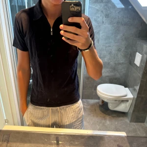 Marinblå pikétröja Tiger of Sweden - Marinblå pikétröja från Tiger of Sweden med kort ärm och klassisk krage. Tröjan har en snygg half zip-dragkedja framtill och är tillverkad i mjuk bomull. Perfekt för dig som gillar stilrena och enkla plagg med en modern touch.