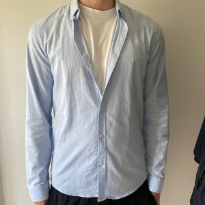 Ljusblå skjorta från Lindbergh - Snygg ljusblå skjorta med klassisk krage och vita knappar. Skjortan har lång ärm och en stilren, enkel design som passar till många olika outfits. Tillverkad i mjuk bomull för en skön känsla hela dagen.