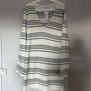 Randig stickad klänning från Nelly - Superfin stickad klänning från Nelly i vitt med svarta ränder. Klänningen har v-ringning, långa ärmar och en avslappnad passform. Perfekt för dig som gillar en enkel men snygg stil.