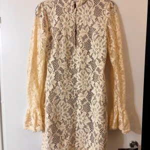Beige spetsklänning från House of CB - Superfin beige spetsklänning från House of CB med långärmade volangärmar och vackert blommigt spetsmönster. Färgen heter oat, strl M tall.