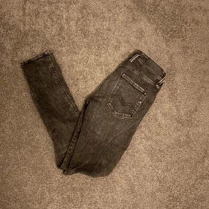 Replay Anbass svarta jeans 30/32 - Säljer ett par svarta Replay Anbass jeans. Jeansen har snygga slitningar, klassiska fem fickor och tydliga Replay-detaljer. Materialet är stretchigt jeans för en bekväm passform. Perfekta för dig som gillar en smal siluett och cool streetstil.