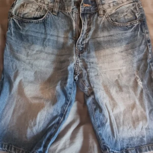 Blå jeansshorts från DSN, storlek 40 - Snygga blå jeansshorts från DSN i storlek 40. Klassisk femficksmodell med slitningar och ljus tvätt för en avslappnad vibe. Shortsens längd går till knäna och de har normal passform. Perfekta för varma dagar och chill stunder.
