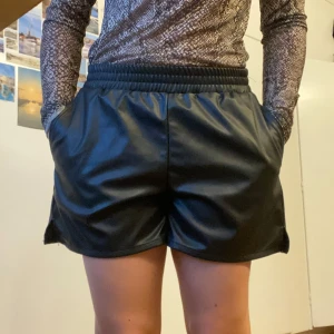 Svarta shorts i skinnimitation - Mjuka svarta shorts i skinnimitation med elastisk midja. I väldigt bra skick-användes några få gånger