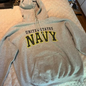 Grå VINTAGE hoodie med NAVY-tryck - Snygg grå VINTAGE hoodie med stor gul och svart NAVY-logga framtill och texten United States. Klassisk känguruficka, huva med snörning och mjukt material. Perfekt för dig som gillar college-stil och oversized look. Fits medium Vintage condition inga flaws
