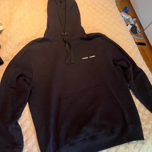 Marinblå hoodie från Samsøe Samsøe - Marinblå hoodie från Samsøe Samsøe med liten vit logga på bröstet. Klassisk modell med huva och snörning, stor känguruficka framtill och långa ärmar. Perfekt för en chill och stilren look. Mjuk bomullskänsla och relaxed fit.