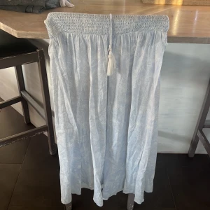 Ljusblå långkjol från Gina tricot/young - Superfin ljusblå långkjol från Gina tricot/young med diskret paisleymönster. Kjolen har smock i midjan och en söt knyt-detalj med tofs. Perfekt för varma dagar och enkel att styla med en crop top eller linne