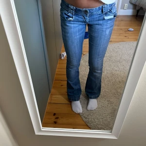 ljusblå bootcut jeans - Lågmidjade bootcut jeans som är justerbara i midjan OBS de är en slitning i rumpan o längst ner på bennet.  MIDJEMÅTT:36cm INNERBENSLÄNGD: 71cm