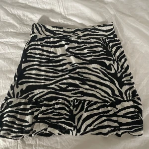 Zebramönstrad kjol  - Snygg kort kjol från Pine Ridge med svartvitt zebramönster och volang längst ner. Kjolen har resår i midjan och är gjord i ett mjukt, lätt tyg som känns skönt mot huden. 