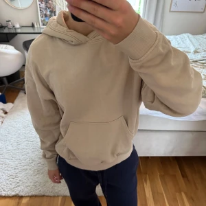 Beige hoodie med huva och ficka - Säljer en stilren beige hoodie med huva och ficka framtill. Tröjan har ribbade muddar vid ärmslut och nederkant, samt snörning i huvan.🥰