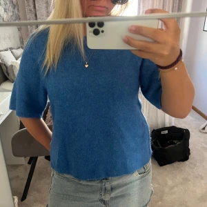 Blå stickad tröja med kort ärm - Säljer en supermjuk blå stickad tröja med korta ärmar och rund hals. Tröjan har en enkel och clean look, perfekt att matcha med jeans eller kjol. Den har en lite boxig passform och är i ett fluffigt material som känns lyxigt. Helt oanvänd med prislapp kvar 