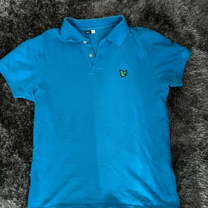 Blå pikétröja från Lyle & Scott - Säljer en blå pikétröja från Lyle & Scott i mycket bra skick. Perfekt för en avslappnad och stilren look.